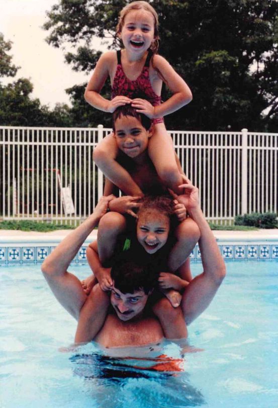 A family having fun together, stacked on their dad’s shoulders in a swimming pool